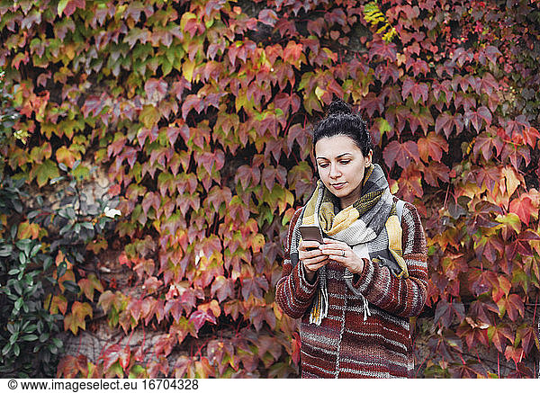 Pretty woman in scarf looking at her cell phone  red autumn leaves