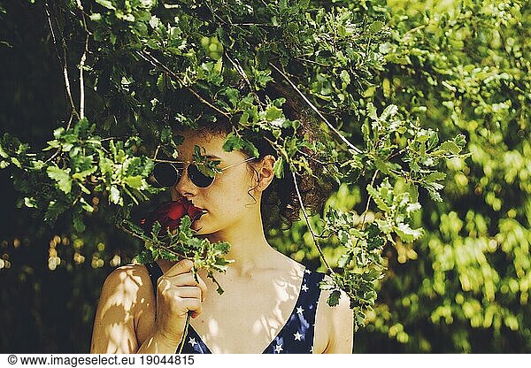 pretty young girl with sunglasses and red rose among branches