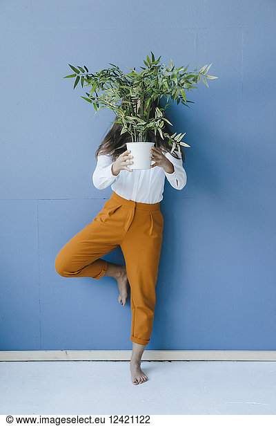 Pretty young woman holding potted plant in front of her face