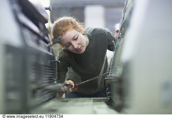 Print worker repairing print machine with screw driver