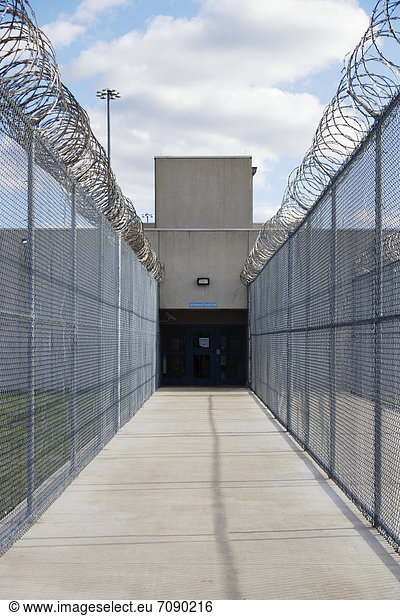 Prison fence and barbed wire at exit of a Correctional Facility. A narrow walkway with high fencing  and coiled razor wire.