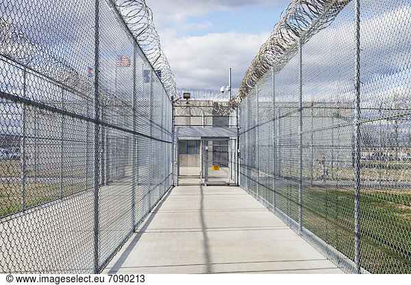 Prison fence  gate and barbed wire at a Correctional Facility. narrow walkway with security fencing.