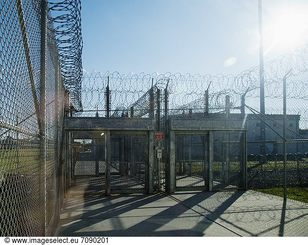 Prison fence  locked gate and barbed wire at Correctional Facility. Prison buildings and exercise yard. High security.