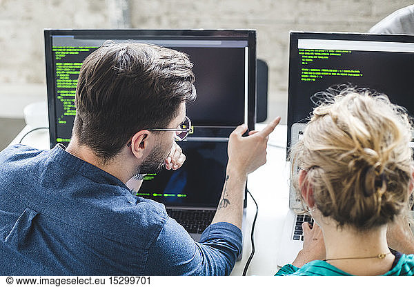 Professional hackers discussing over computer codes on monitor in creative office