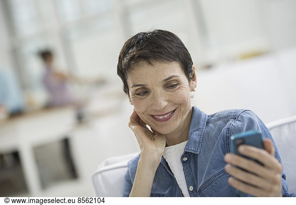 Professionals in the office. A light and airy place of work. A mature woman in a blue denim shirt looking at a blue smart phone.