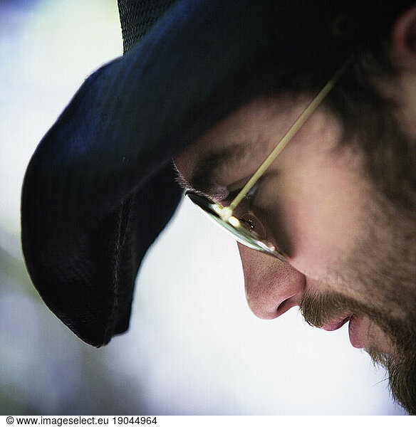 Profile of a bearded young man wearing a black hat and sunglasses.