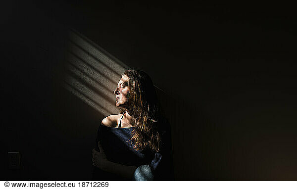 Profile of a woman sitting in a patch of light in a darkened room.