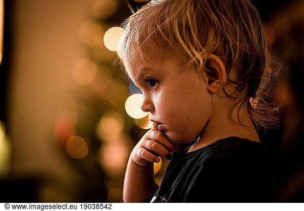 profile of baby/toddler with finger in mouth and bokeh lights