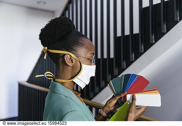 Profile of businesswoman wearing protective mask looking at color sample in staircase