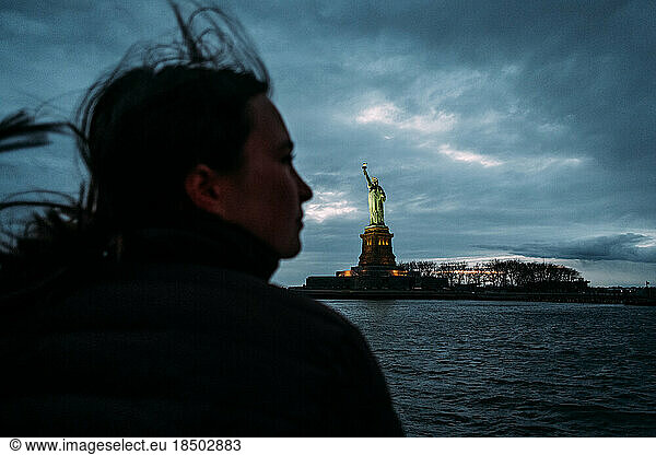 Profile of girl looking at statue of liberty at dusk