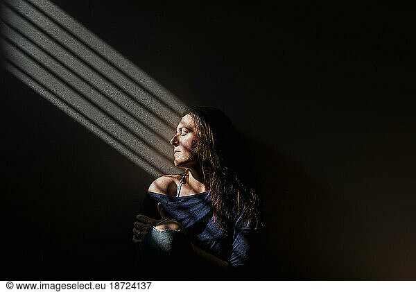 Profile of woman with eyes closed in a patch of light a dark room.