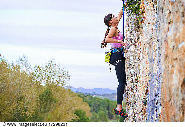 Profile photo of a young woman climbing a steep rock wall