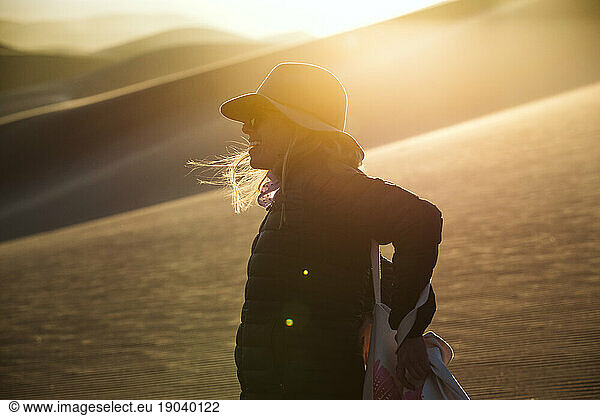 profile portrait of a female adventurer in felt hat at sunset in dunes