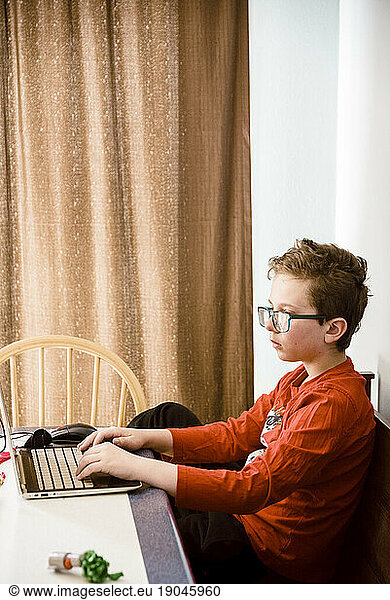Profile shot of a boy working on a laptop studying at the table.