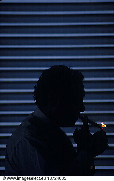 Profile view in silhouette of the former chairmen of a large financial company lighting a cigar.