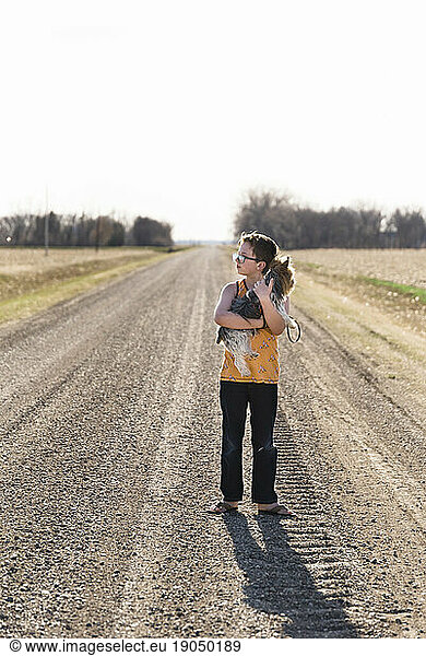 Profile view of a boy holding his pet dog on a gravel road.