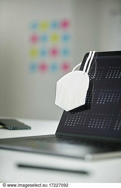 Protective face mask hanging on laptop in office