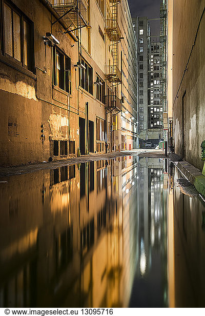 Puddle on alley amidst buildings at night during rainy season