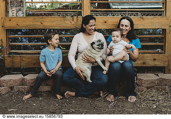 Pug  brother and two moms laughing at baby girl outdoors