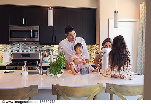 Pull back of young family of four baking together in the kitchen.