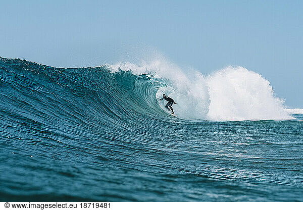 Pulled back view of a surfer in a barrel against a blue sky