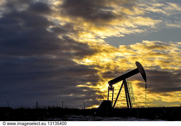 Pumpjack at oil industry against cloudy sky during sunset
