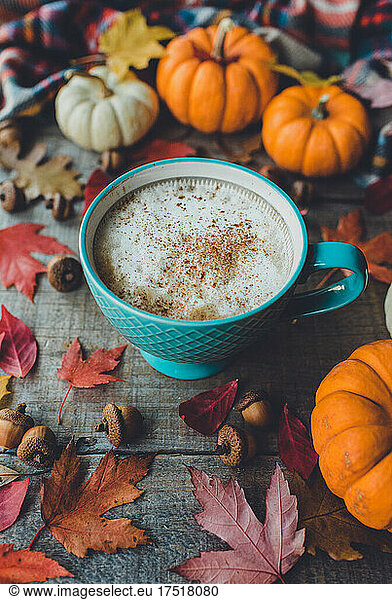 Pumpkin spice latte on wooden table with leaves and pumpkins.