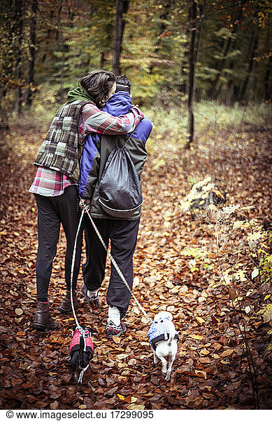 queer female couple hug and walk dogs in golden leaves in forrest