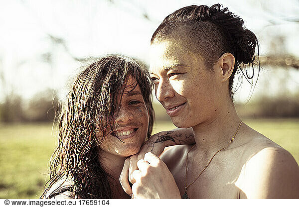Queer women couple smiling in embrace on a warm day in nature