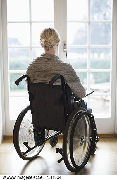 Rückansicht der behinderten Frau im Rollstuhl gegen Fenstertüren