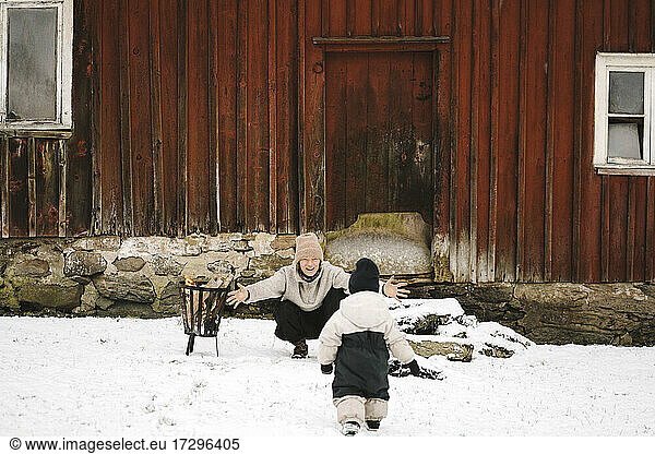 Rückansicht der Tochter  die auf die Mutter zuläuft  auf Schnee gegen die Hütte