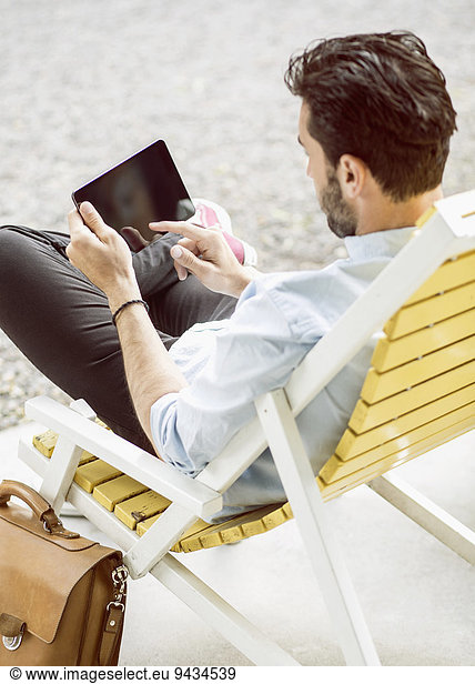 Rückansicht des Geschäftsmannes mit digitalem Tablett auf Lounge Chair im Park