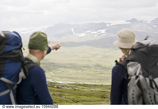 Rückansicht des Wanderers  der auf die Berge zeigt  während er neben einem Freund steht.