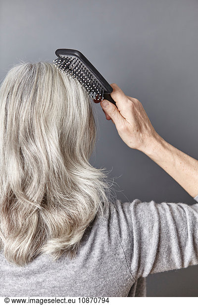 Rückansicht einer Frau  die lange graue Haare bürstet