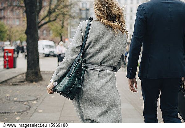 Rückansicht einer Geschäftsfrau mit Handtasche beim Spaziergang eines Kollegen in der Stadt