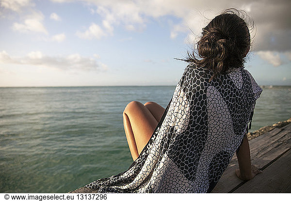 Rückansicht einer in eine Decke gehüllten Frau  die sich auf einer Strandpromenade am Meer entspannt