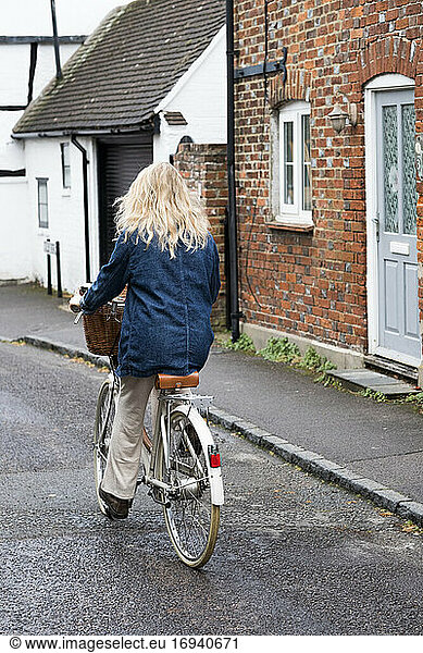 Rückansicht einer jungen blonden Frau beim Radfahren auf einer Dorfstraße.