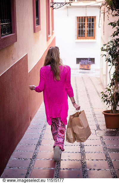 Rückansicht einer Touristin  die mit Einkaufstaschen durch eine Gasse schlendert  Marbella  Spanien
