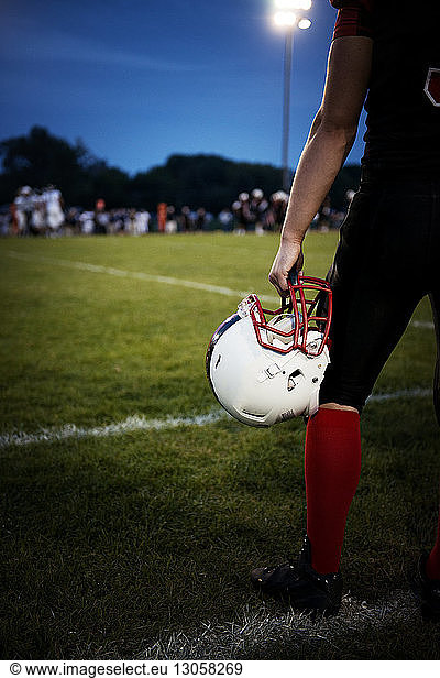 Rückansicht eines American-Football-Spielers  der einen Helm hält und auf dem Football-Feld steht