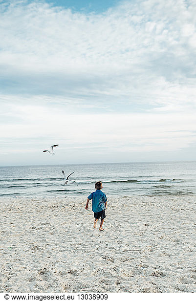 Rückansicht eines Jungen  der am Strand von Panama City gegen bewölkten Himmel läuft