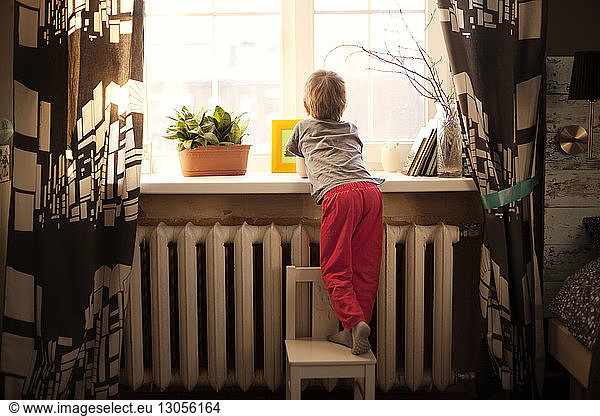 Rückansicht eines Jungen  der zu Hause auf einem Stuhl am Fenster steht