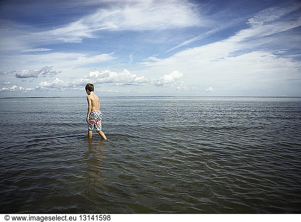 Rückansicht eines Jungen ohne Hemd  der im Meer gegen den Himmel läuft