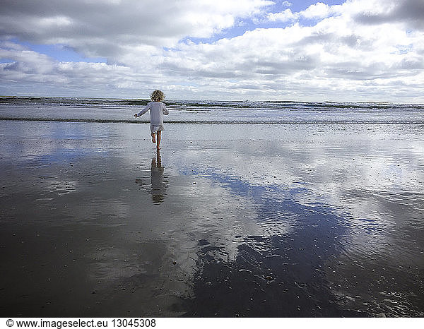 Rückansicht eines Mädchens  das am St. Augustine Beach gegen bewölkten Himmel läuft