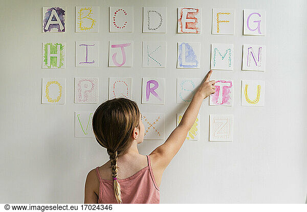 Rückansicht eines Mädchens (8-9)  das das Alphabet an der Wand betrachtet