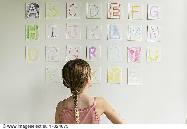 Rückansicht eines Mädchens (8-9)  das das Alphabet an der Wand betrachtet