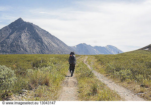 Rückansicht eines männlichen Wanderers auf einem Wanderweg inmitten eines Feldes gegen den Himmel