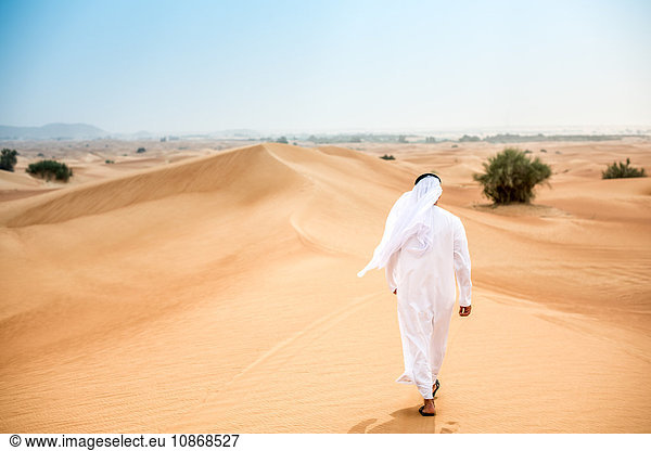 Rückansicht eines Mannes aus dem Nahen Osten  der in traditioneller Kleidung in der Wüste spazieren geht  Dubai  Vereinigte Arabische Emirate