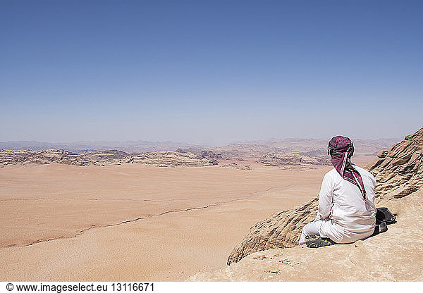 Rückansicht eines Mannes  der auf einem Felsen sitzt und die Aussicht betrachtet