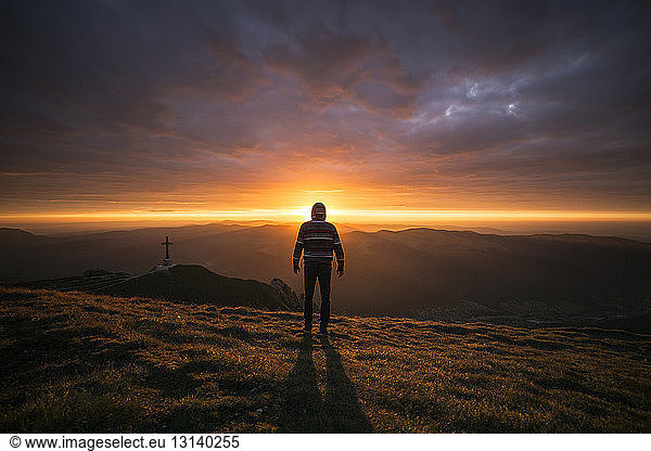 Rückansicht eines Mannes  der bei Sonnenuntergang auf einem Berg steht