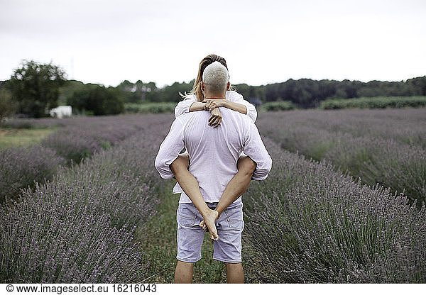 Rückansicht eines Mannes  der eine Frau auf einem Lavendelfeld hält